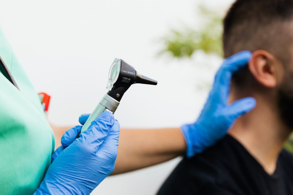 a-person-holding-heine-otoscope-5206950 Healthcare professional examining patients ear with an otoscope in a clinical setting.